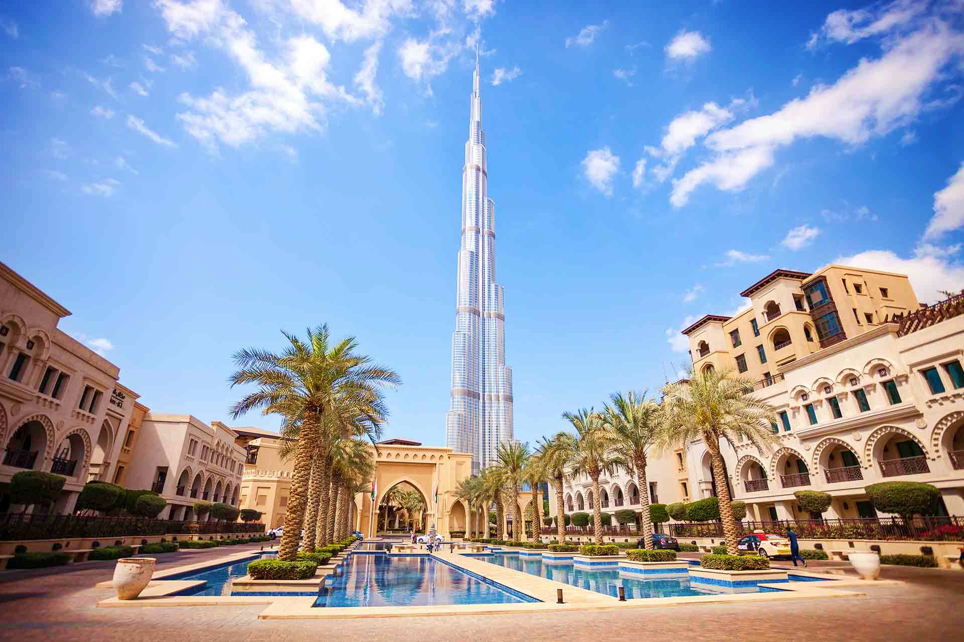 Burj Khalifa tower rising above Downtown Dubai plaza with reflecting pool, palm trees, and traditional Arabic architecture bu